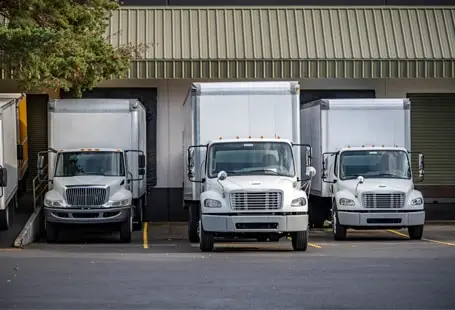 Fleet of white commercial box trucks at a warehouse loading dock