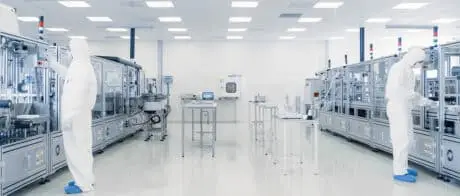 Scientists in sterile protective gear working on a high-tech assembly line inside a pharmaceutical or semiconductor cleanroom.