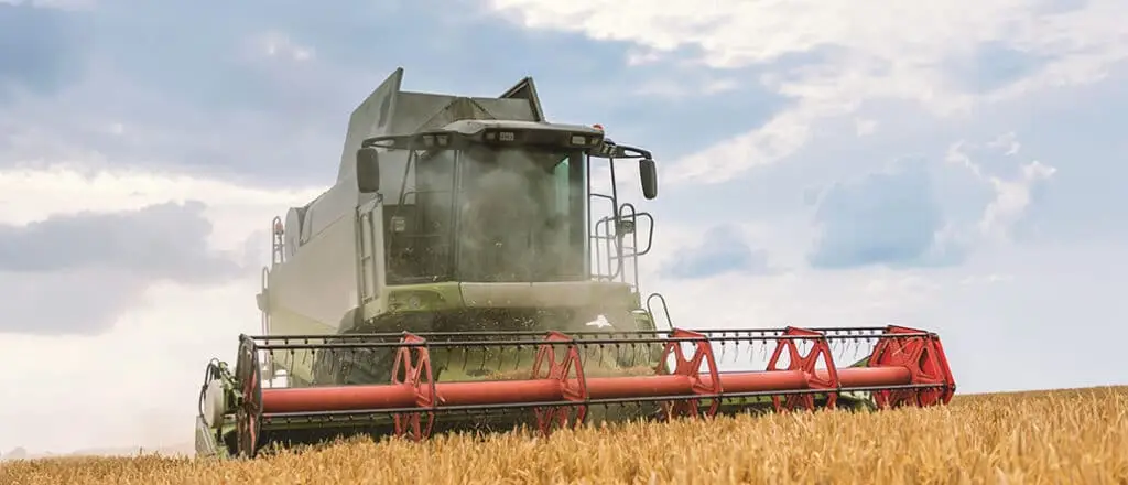 Modern agricultural field equipment, a combine harvester, working in a wheat field, representing a major capital investment for a farming operation.