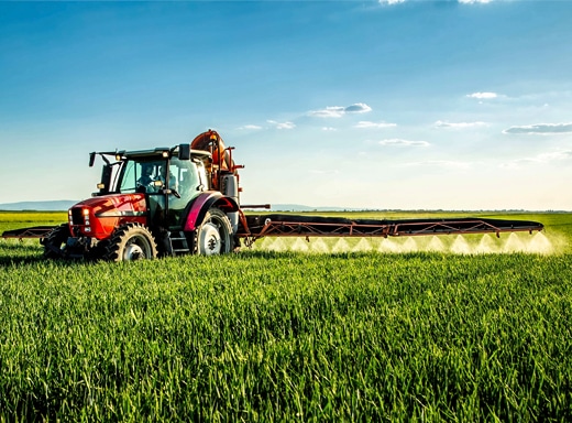 Red tractor spraying a lush green farm field, representing a $3.6 million agriculture rental fleet financing case study by Commercial Funding Partners.
