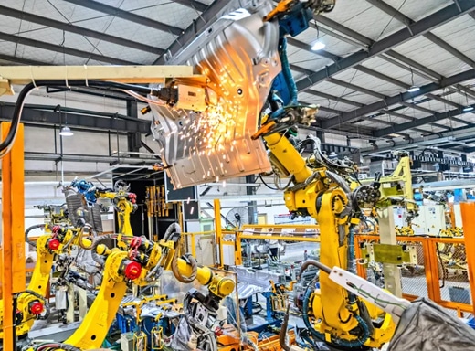 arge yellow automated robots generating sparks while welding a heavy metal component in a manufacturing plant.
