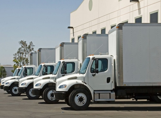 Fleet of identical white commercial box trucks lined up at a logistics and mail facility.