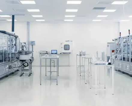 Scientists in sterile protective gear working on a high-tech assembly line inside a pharmaceutical or semiconductor cleanroom.